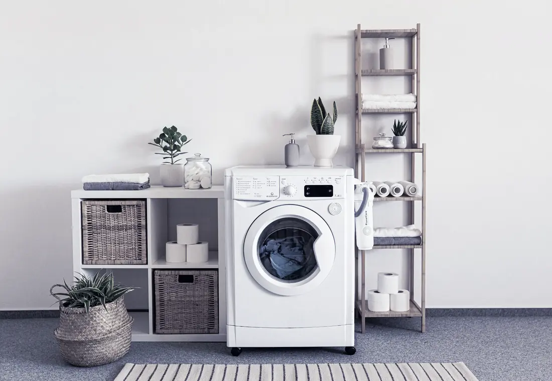A white washing machine in a bright utility room with shelves and baskets